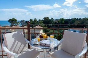 A balcony with two chairs, a table with breakfast items, and a view of the sea and greenery. - Socrates Studios (Kefalonia)