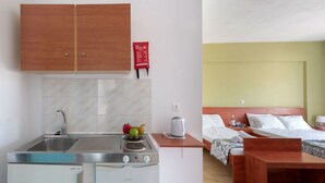 A compact hotel room with a kitchenette, a bed with two pillows, a bedside table, and a small wooden bench. - Socrates Studios (Kefalonia)