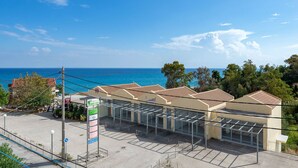 A coastal hotel with a sea view, a parking lot, and a sign indicating a restaurant. - Socrates Studios (Kefalonia)