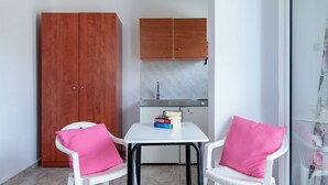 A small kitchenette with a sink and cabinets, two white chairs with pink cushions, and a white table. - Socrates Studios (Kefalonia)