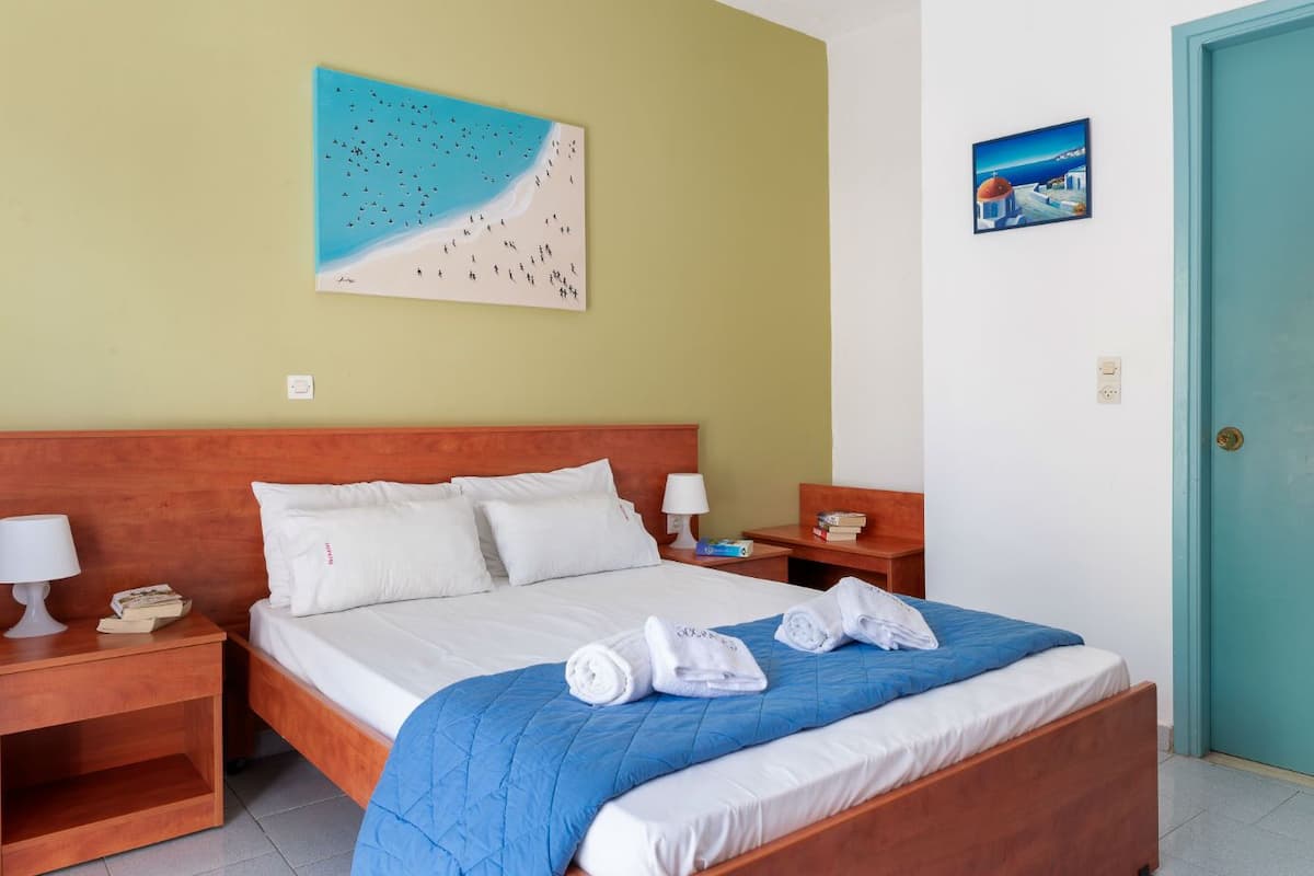 A hotel room with a wooden bed, white bedding, a blue quilt, and two nightstands with lamps and books.