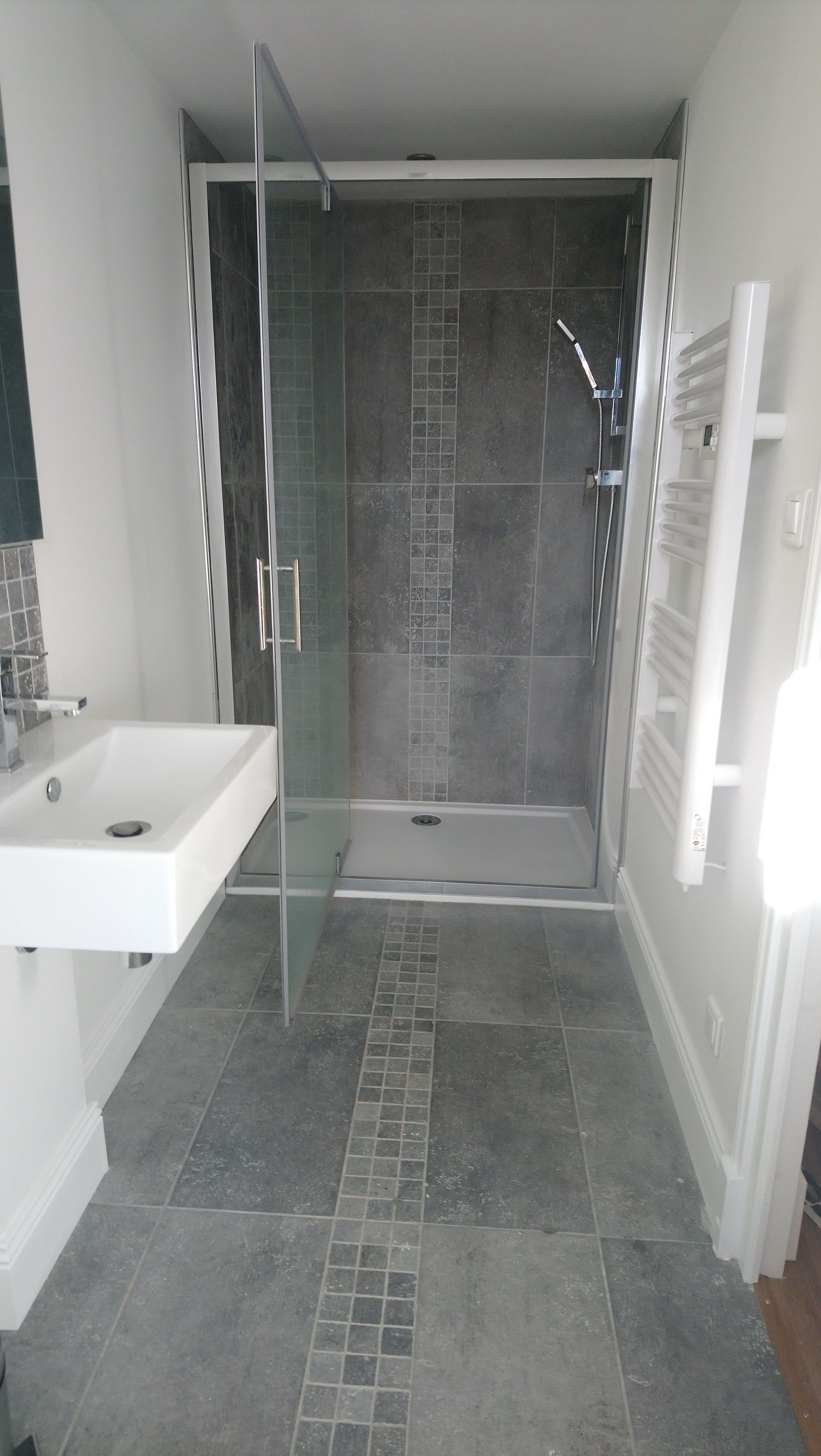 Une salle de bain moderne avec une douche à parois de verre, un lavabo blanc et un sol carrelé.