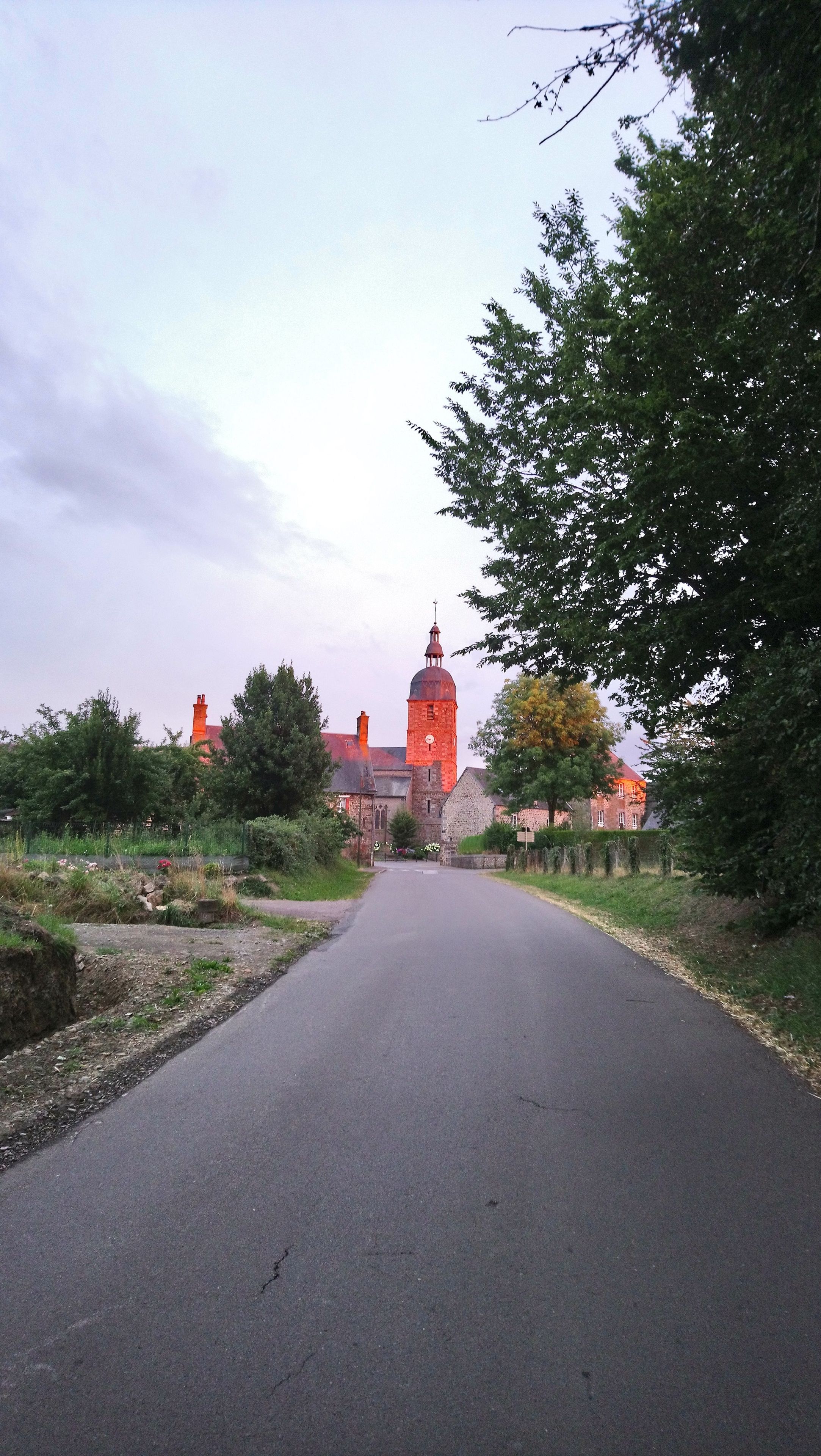 A rural road leading to a church with a prominent tower and clock.