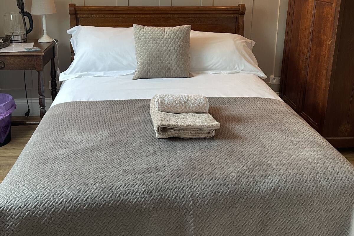 A neatly made bed with a folded towel, a wooden headboard, and two wall-mounted lights.