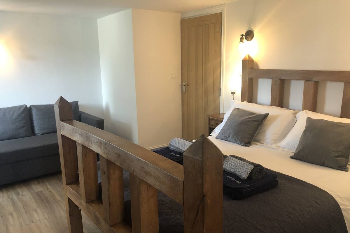 A room with a bed, a wooden headboard, a nightstand, a lamp, and a sofa.