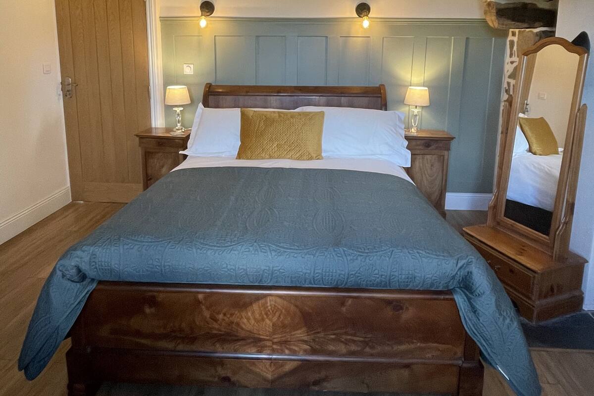 A bedroom with a wooden bed, two bedside tables with lamps, a wooden wardrobe, and a large mirror.