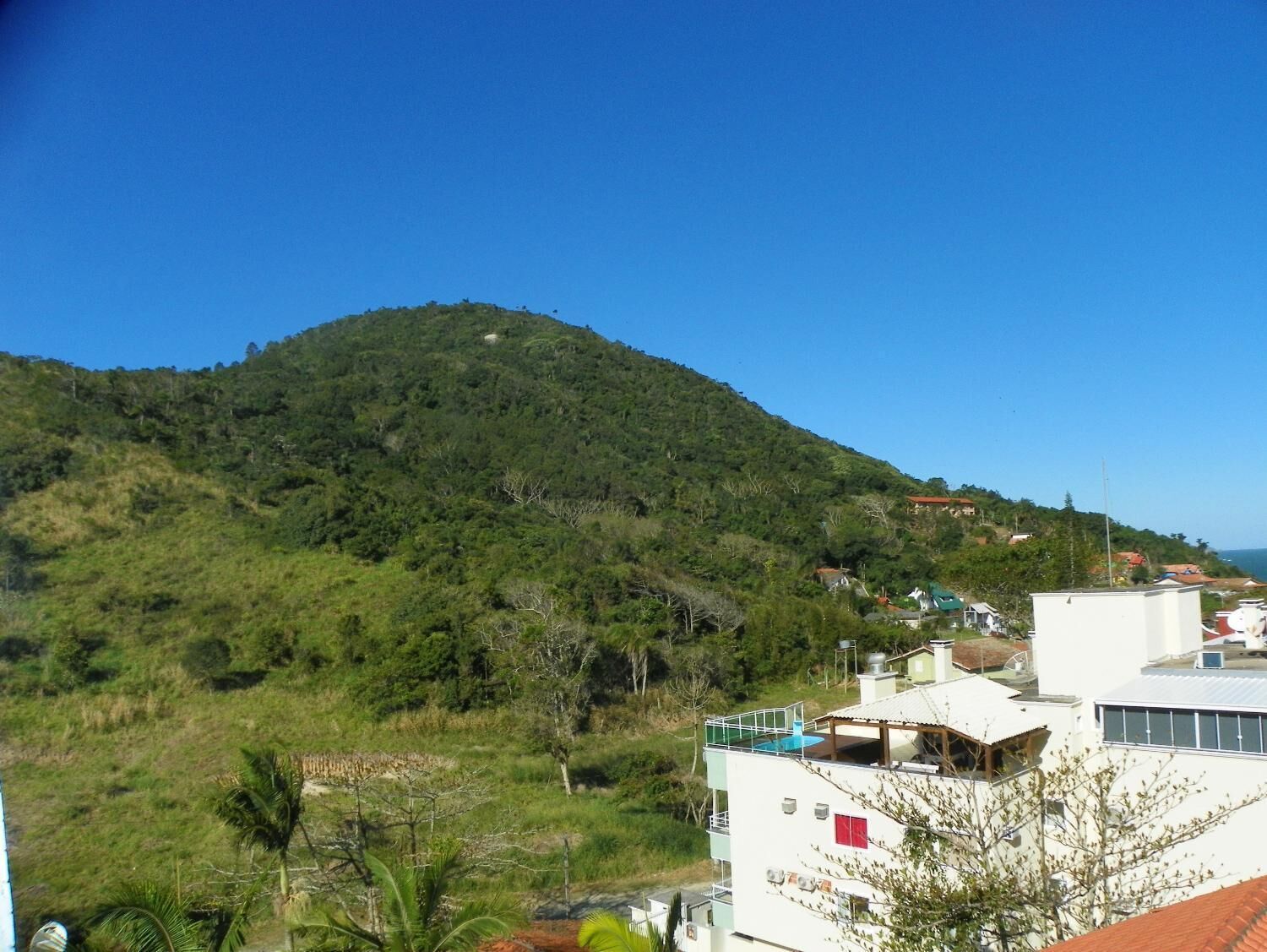 Une colline sur laquelle se trouve un bâtiment doté d’une piscine sur le toit et offrant une vue sur la mer.