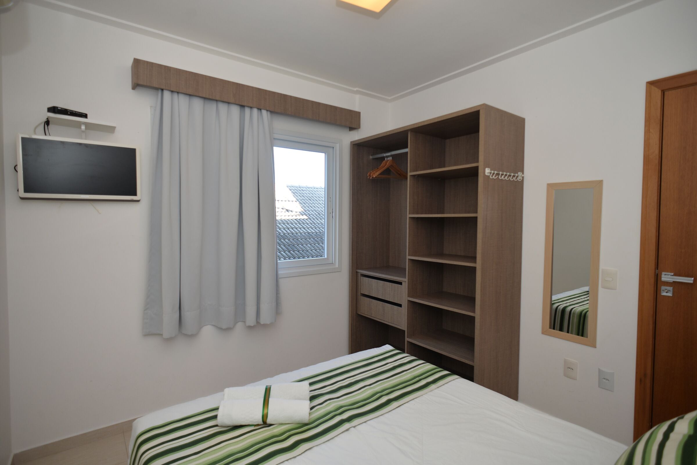 A bedroom with a bed, a TV, a wardrobe, and a window with curtains.