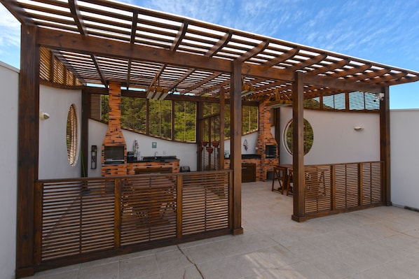 An outdoor patio area with a wooden pergola, a brick fireplace, and a seating area.