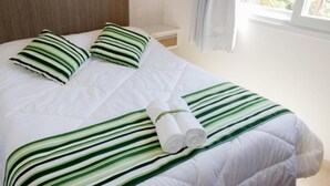 A neatly made bed with green and white striped bedding, two pillows, and rolled towels. - Pousada Villa Maciel (Bombinhas)