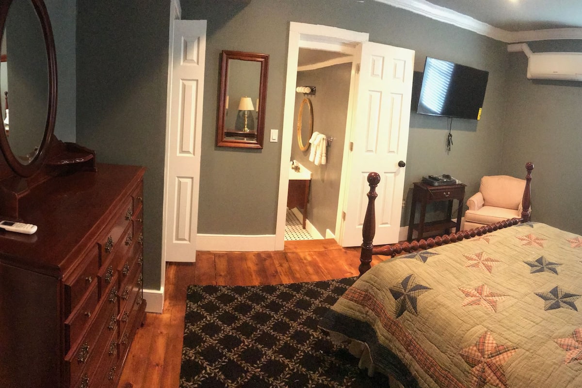 A bedroom with a bed, dresser, mirror, and a television on the wall.