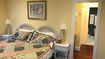 Un dormitorio con una cama, dos mesitas de noche, una lámpara, un cuadro enmarcado y un cesto de ropa.