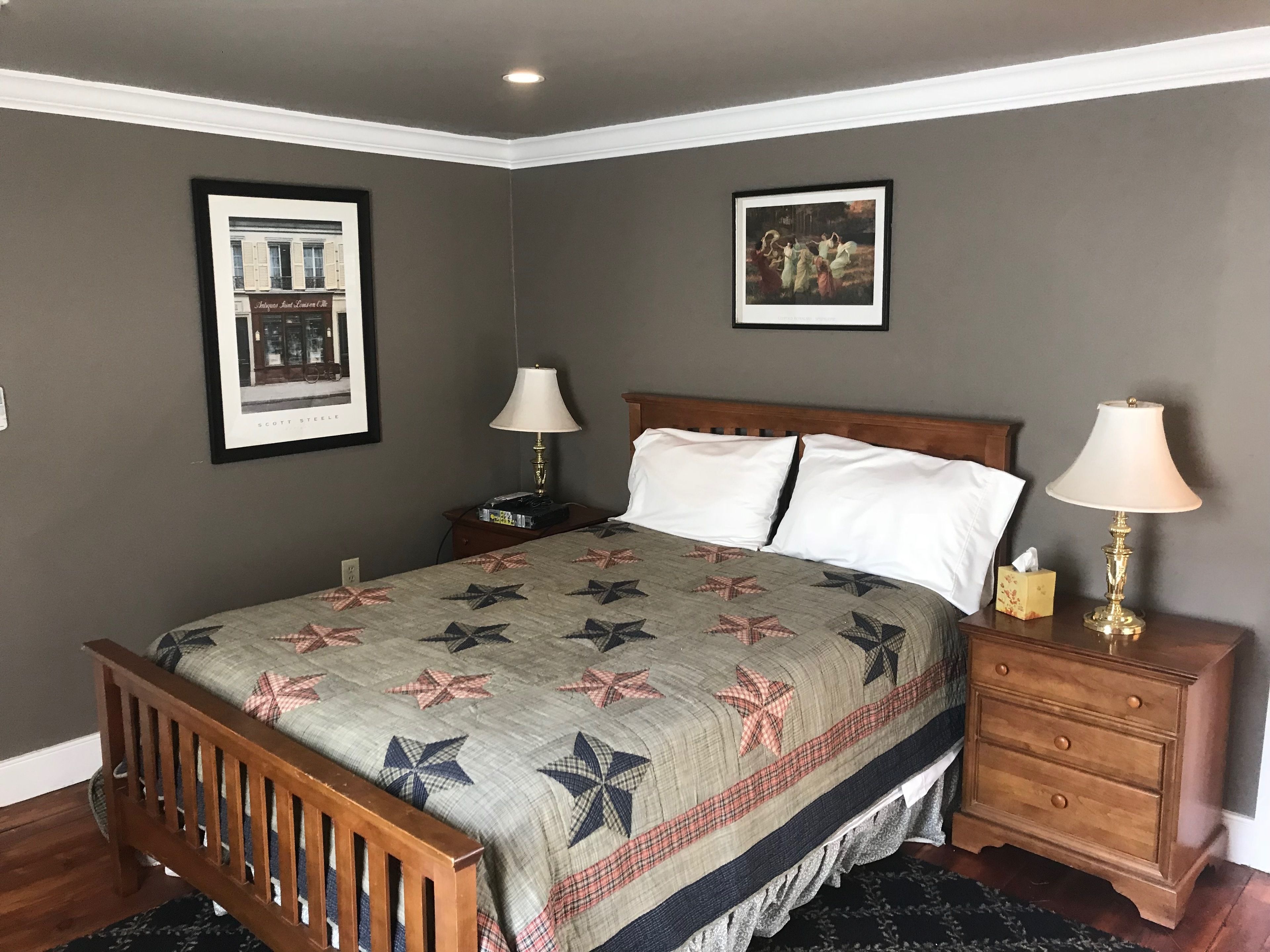 A bedroom with a wooden bed, two bedside tables with lamps, a nightstand, and two framed pictures on the walls.