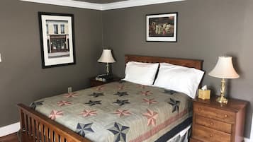 A bedroom with a wooden bed, two bedside tables with lamps, a nightstand, and two framed pictures on the walls.