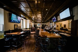 A bar area with multiple seating options, including bar stools and tables, and a television screen displaying sports content. - Stottsville Inn (Coatesville)