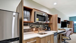 A modern kitchen with a stainless steel refrigerator, microwave, and sink. There is a wooden countertop and a built-in coffee maker.