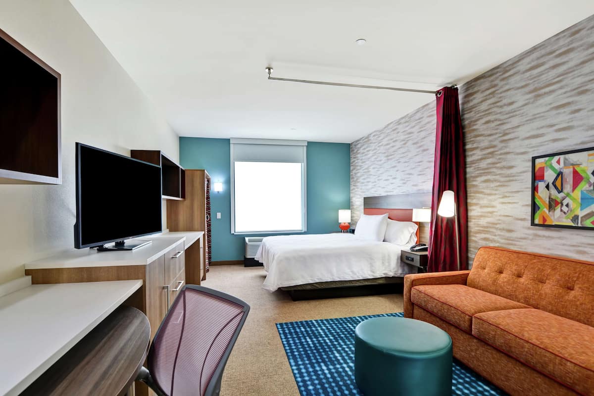 Habitación de hotel con cama, televisión, escritorio, silla, sofá y ventana.