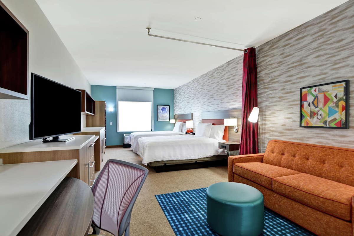 Una habitación de hotel con una cama, un escritorio con televisor de pantalla plana, un sofá, una silla y un ventanal grande.