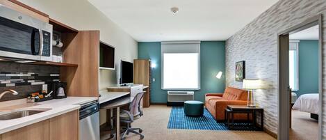 A compact hotel room with a kitchenette, a desk, a comfortable sofa, and a bed.