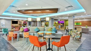 A modern hotel lobby with a central seating area, a bar, and a children's play area.