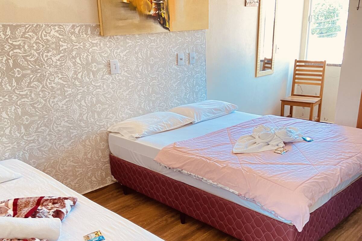 A hotel room with two beds, a wooden floor, a patterned wallpaper, and a window with a view.