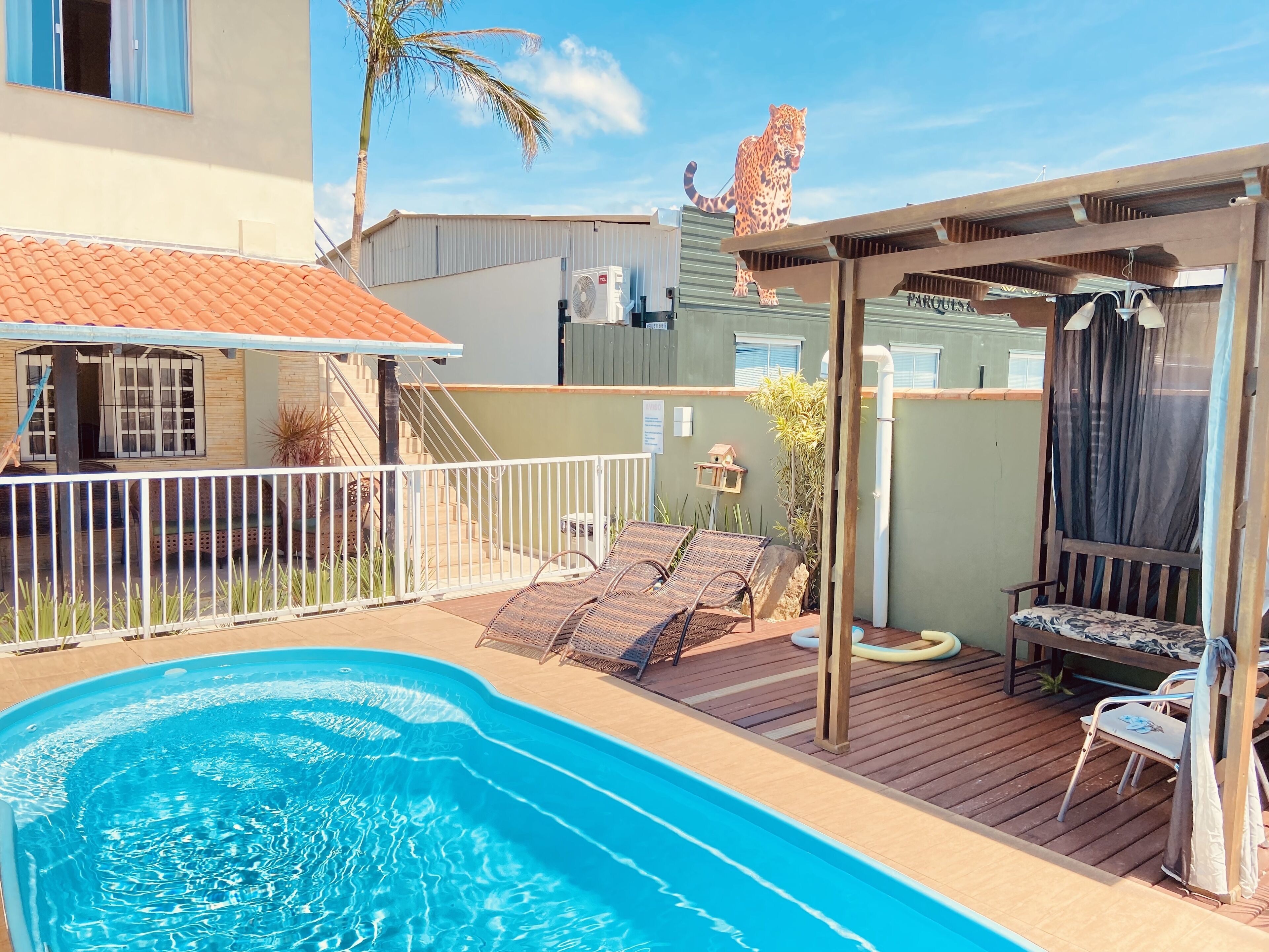 A swimming pool with lounge chairs and a pergola, surrounded by a fenced patio area.