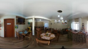A spacious dining area with multiple wooden tables and chairs, a kitchen area with a stove and sink, and a bar area with a counter and stools. - Pousada Mar de Almirante (Penha)