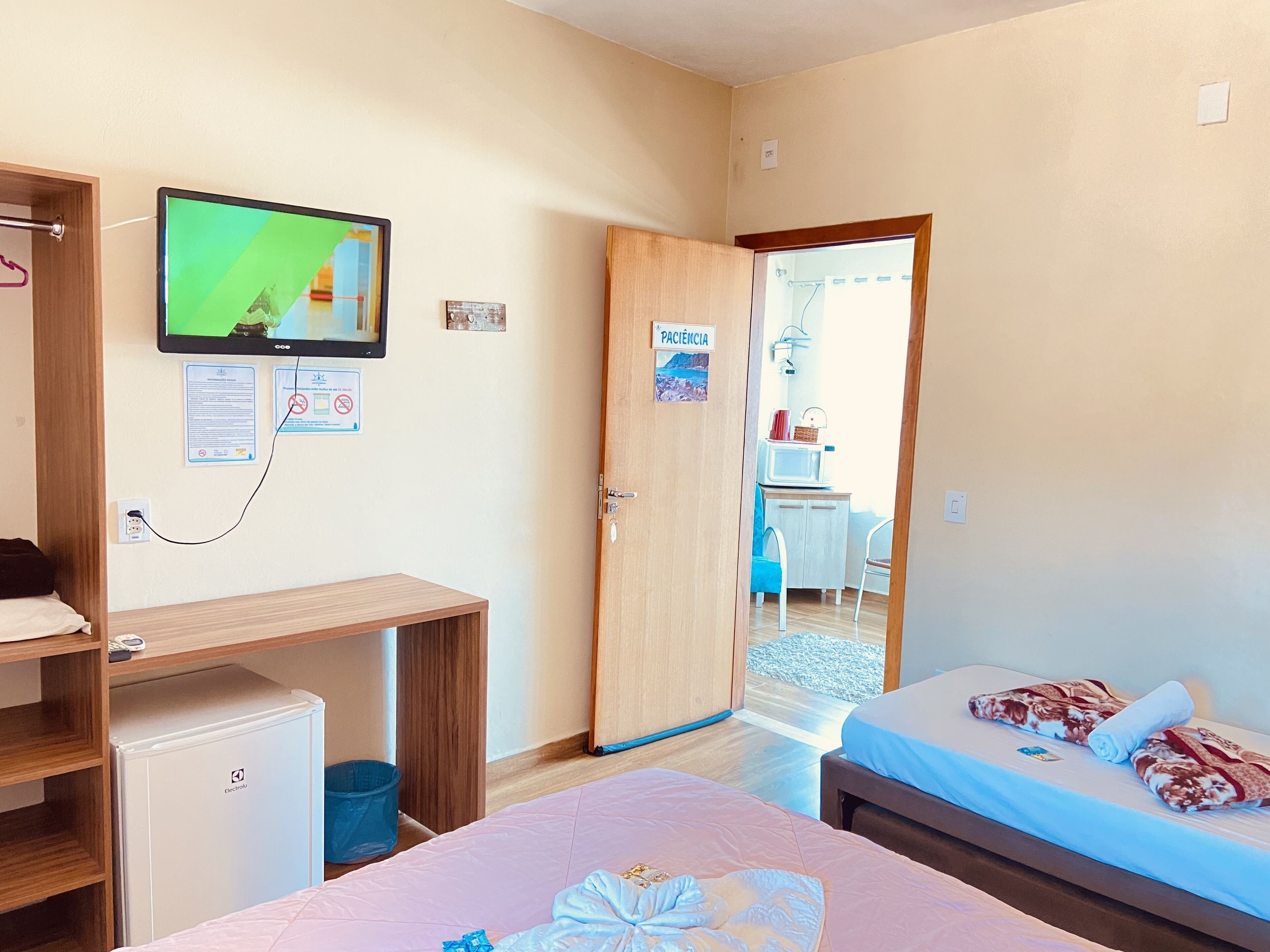 A hotel room with two beds, a desk, a TV, and a door leading to a balcony.