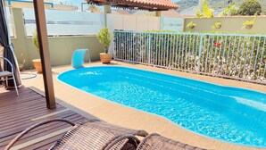 Una piscina con terraza de madera y sillones de mimbre.