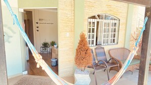 A hammock in a covered outdoor area with wicker furniture and a potted plant. - Pousada Mar de Almirante (Penha)
