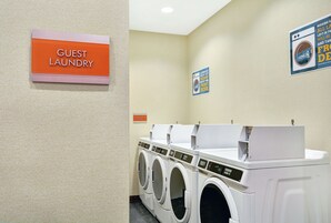 Zona de lavandería para huéspedes con un cartel que indica su ubicación, varias lavadoras y un cartel para la sala de máquinas.