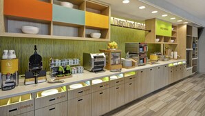 A breakfast bar with a variety of food items and utensils, including a waffle maker and coffee machines.