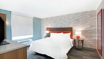 A hotel room with a bed, a desk, a lamp, and a window.