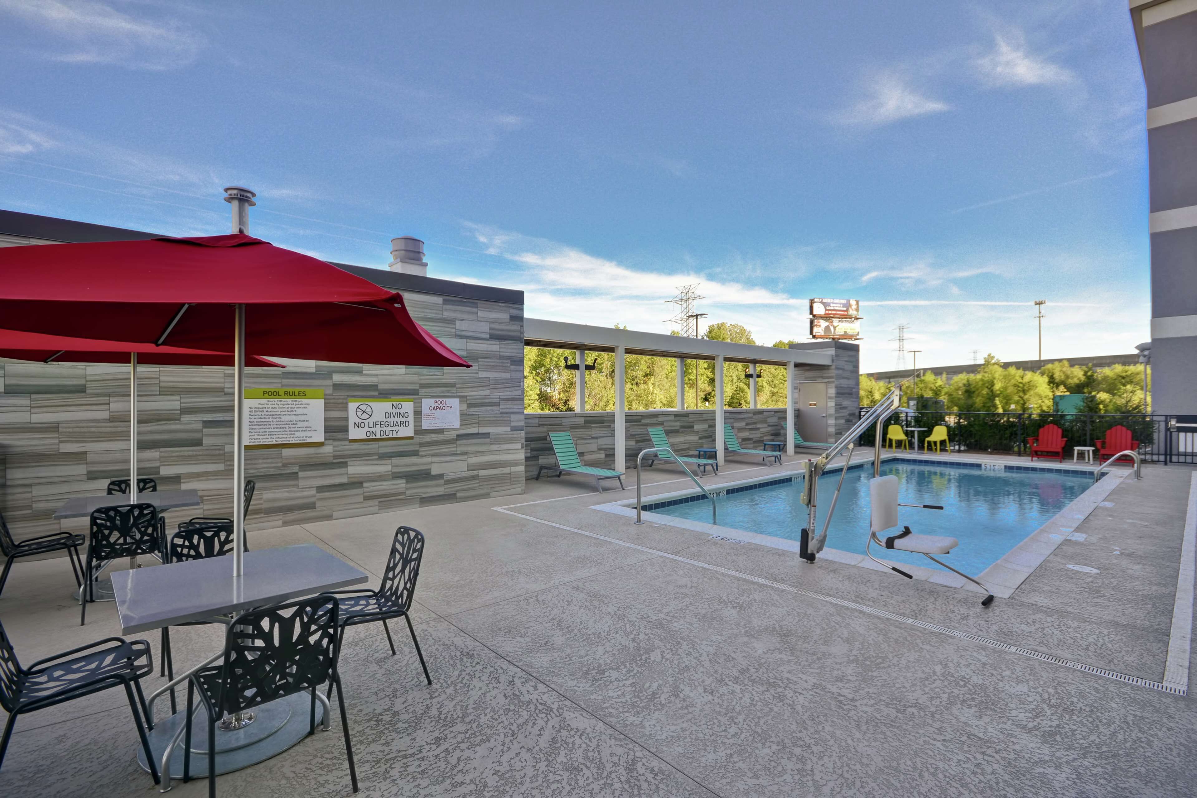 An outdoor pool area with a red umbrella, poolside chairs, and a sign indicating pool rules.
