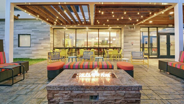 An outdoor patio with a fire feature, seating, and a covered area with string lights.