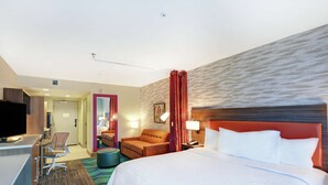A hotel room with a large bed, a desk with a computer, a chair, a TV, and a bathroom visible through an open door.