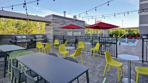 An outdoor patio with tables and chairs, string lights, and a barbecue grill.