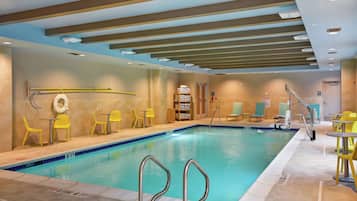 Une piscine intérieure avec des lignes de démarcation bien visibles, des chaises jaunes et un sol carrelé.