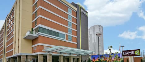 A multi-story hotel with a modern design, featuring a prominent "HOME 2" sign, a covered entrance, and a landscaped area with plants.