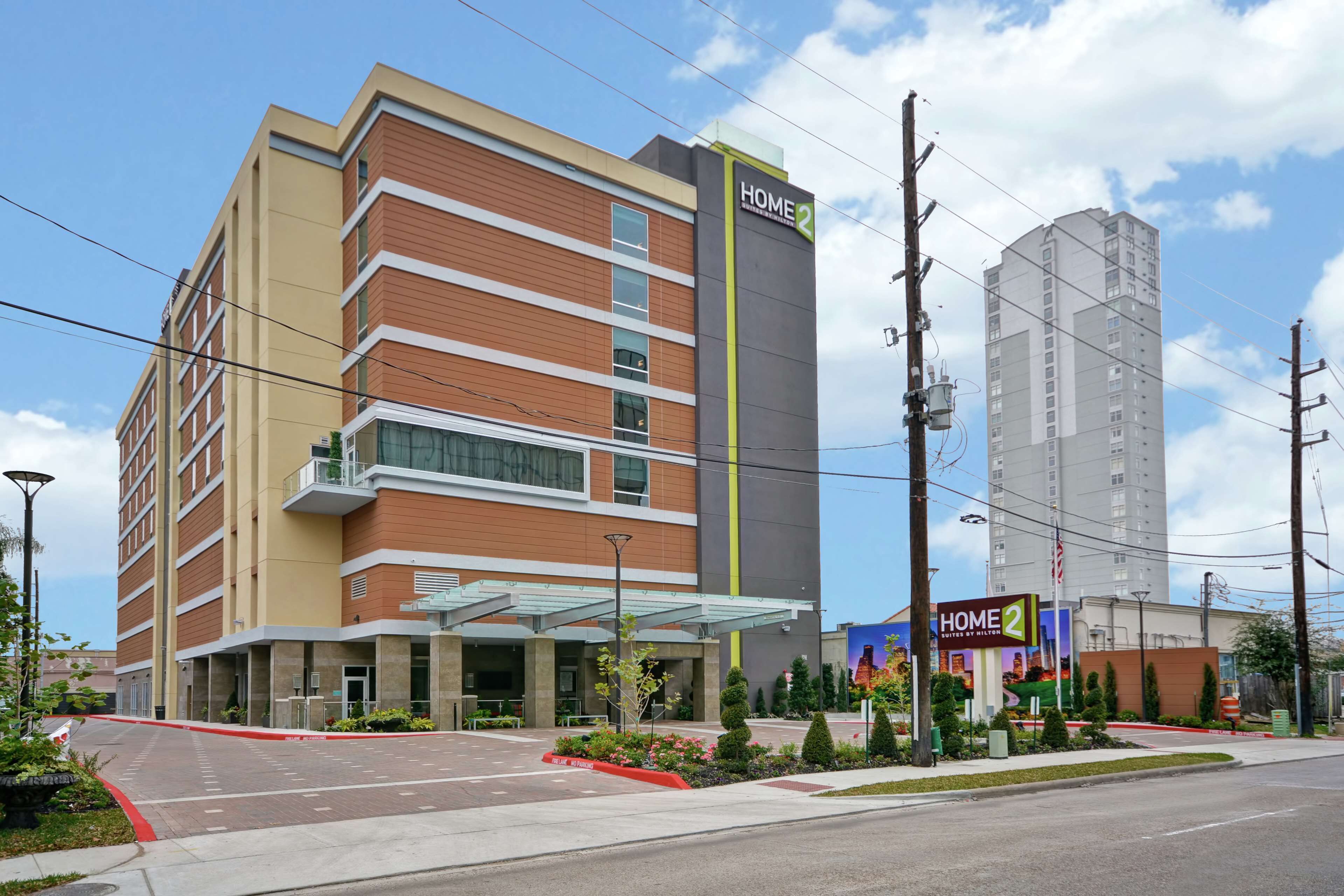 A multi-story hotel with a prominent 'HOME 2' sign, a covered entrance, and a landscaped area with shrubs and a red curb.