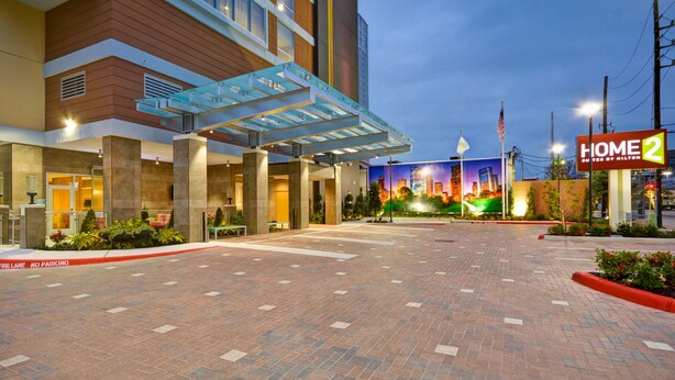 Een hotelingang met een overdekte doorgang, een 'Geen Parkeren'-bord en een bord met 'Home 2 Suites by Hilton'.