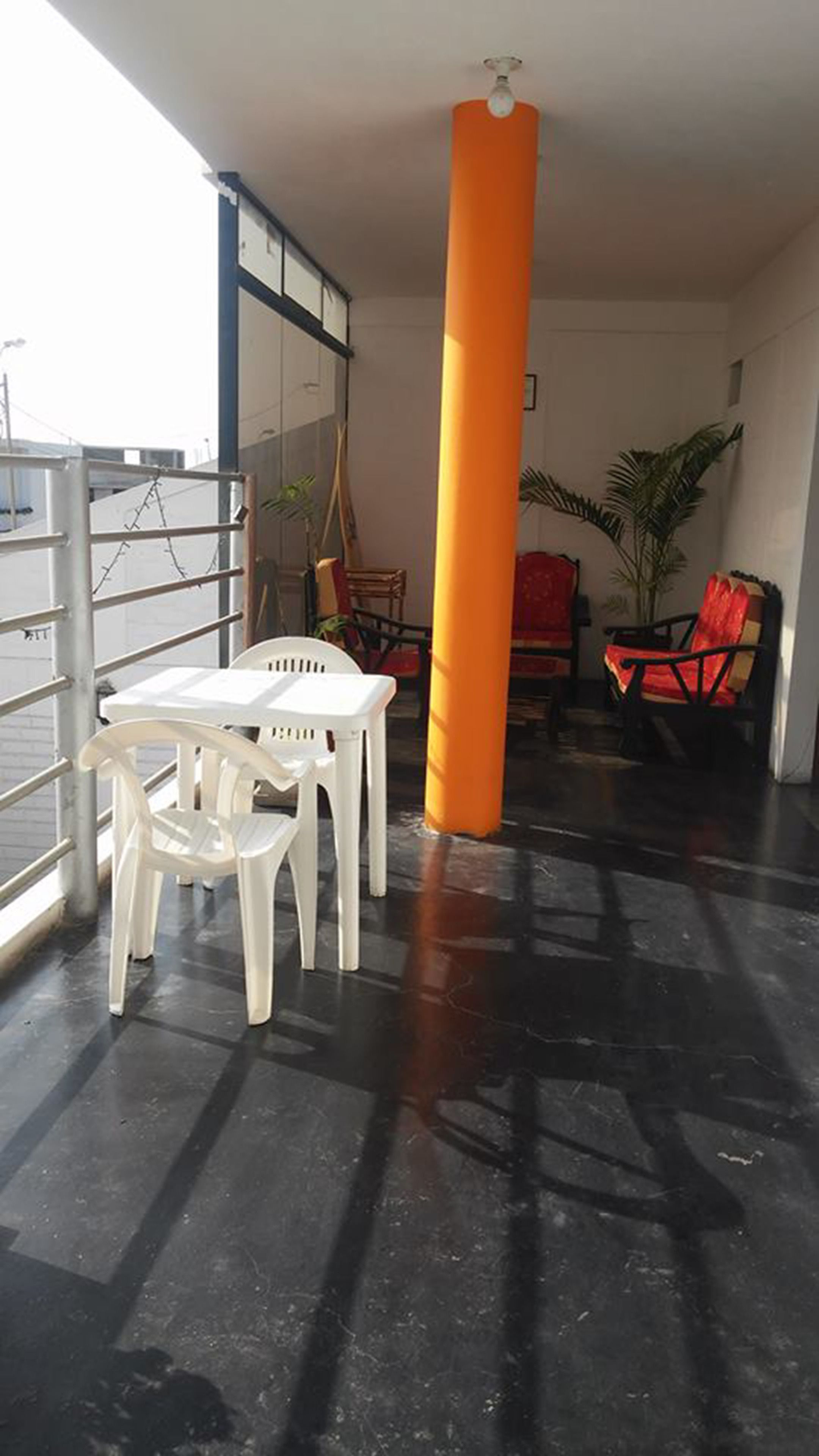 A room with a black floor, white plastic chairs, a red chair, and a large orange pillar.