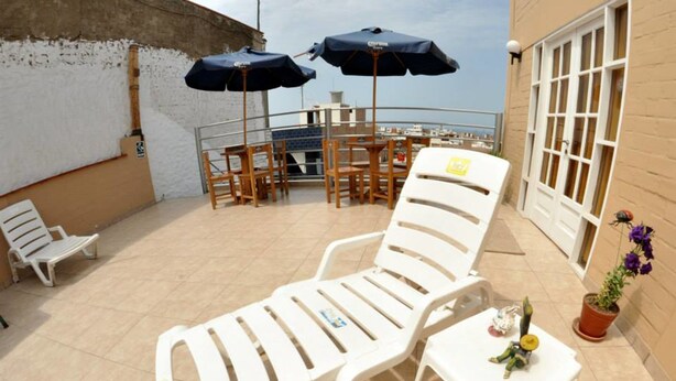 Ligstoel met een tafel, twee parasols en een bloempot op een balkon.