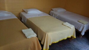 Een kamer met drie eenpersoonsbedden, elk voorzien van een wit kussen en een opgevouwen witte handdoek.