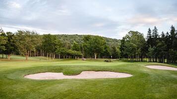 A golf course with sand bunkers, a well-maintained green, and a forested hill in the background.