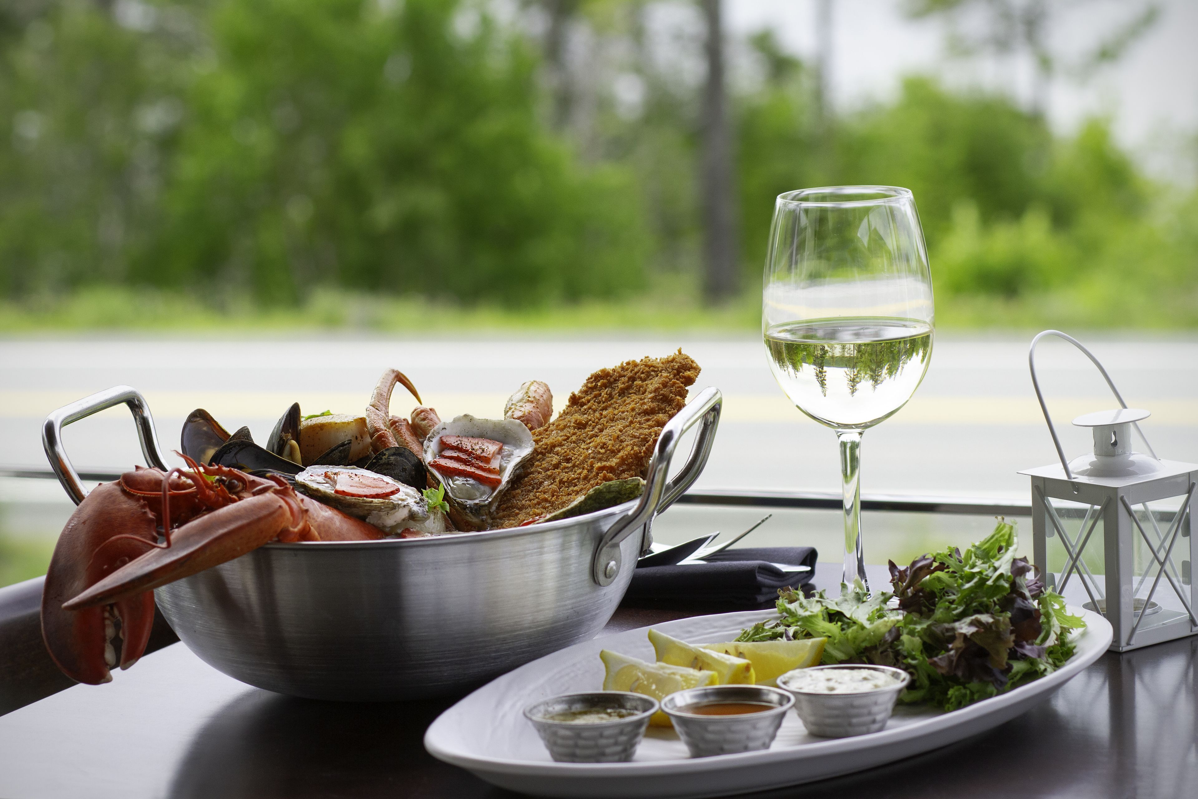 A meal with seafood, breaded items, and a glass of white wine on a table with a scenic view.