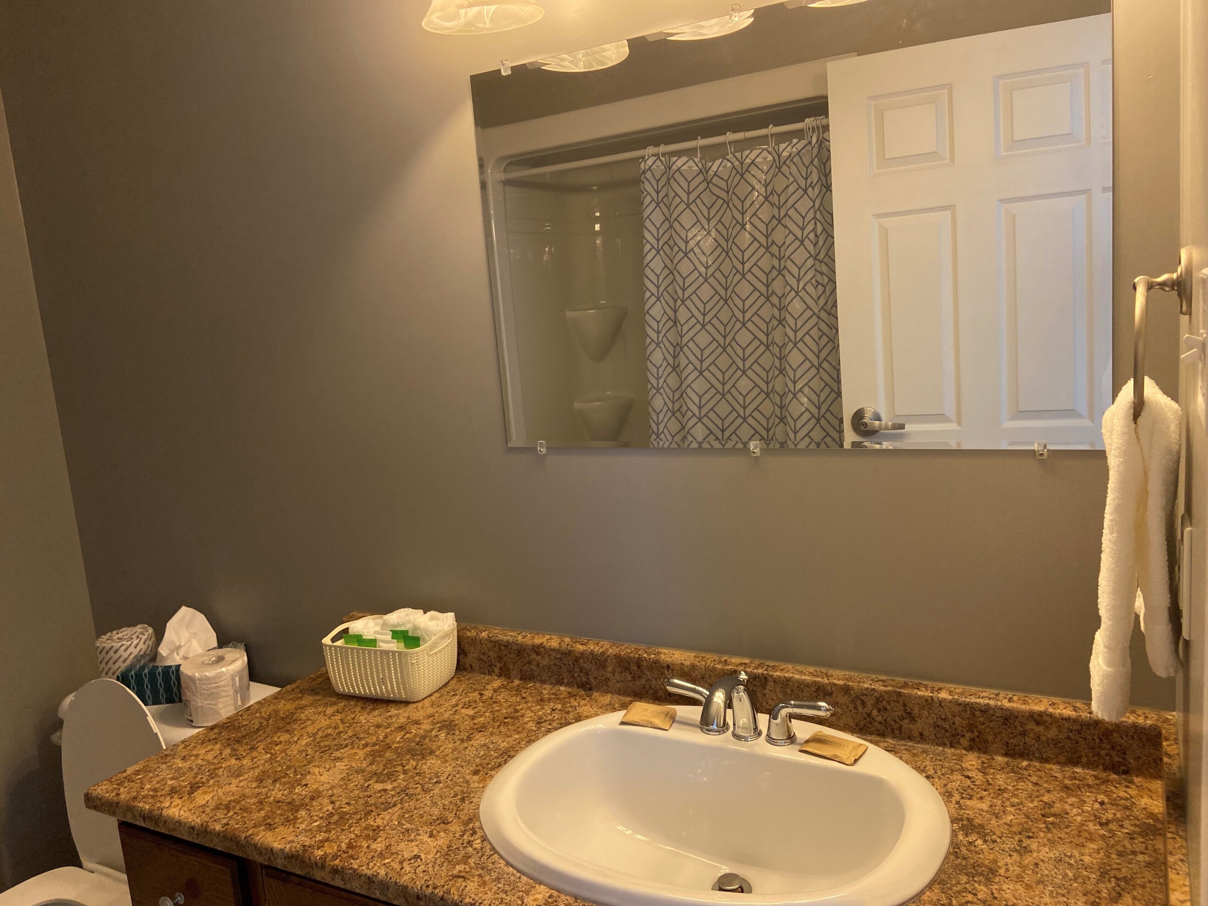 A bathroom with a granite countertop, a white sink, a mirror, and a towel rack.