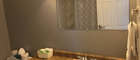 A bathroom with a granite countertop, a white sink, a mirror, and a towel rack.