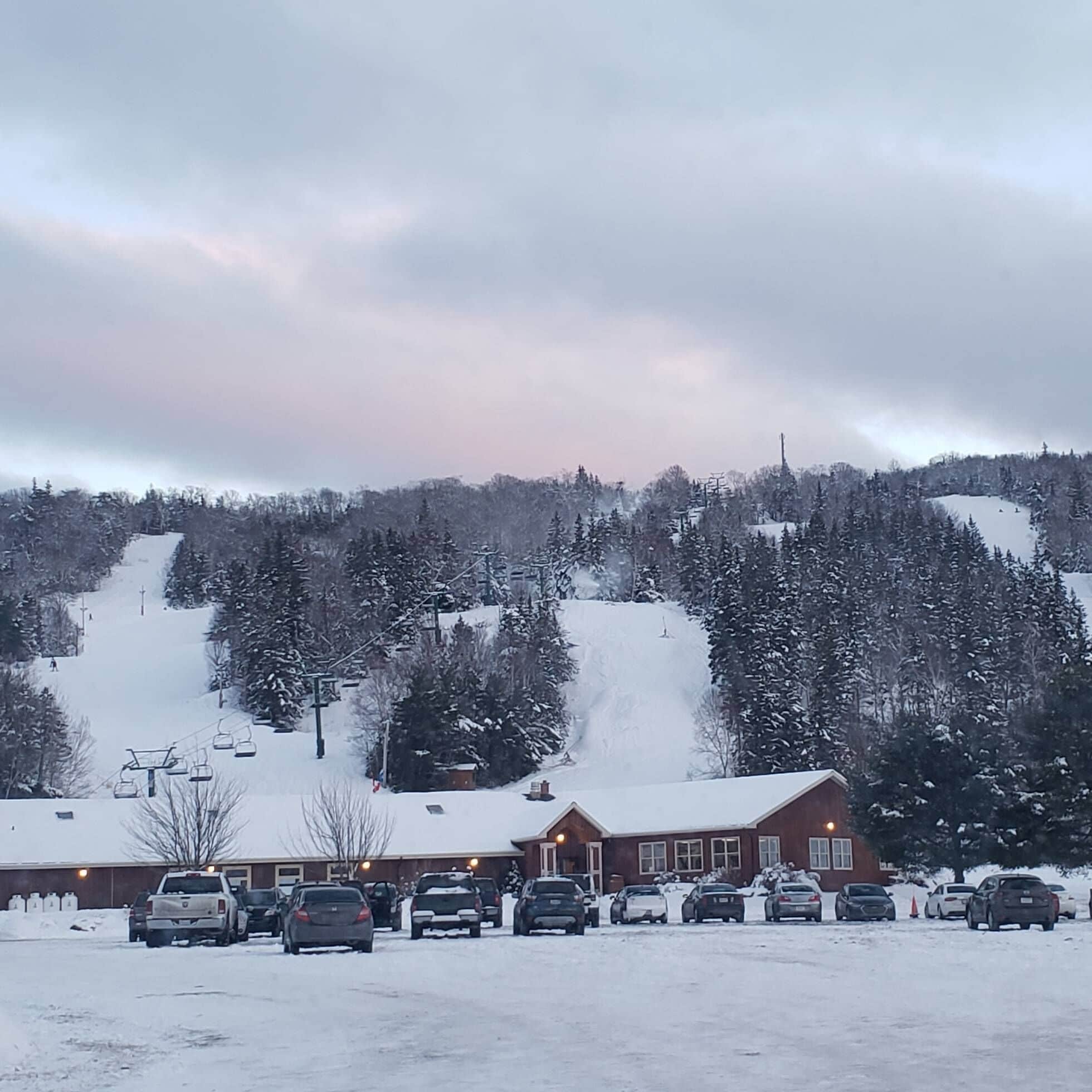 A ski resort parking lot with a building in the foreground and a ski lift in the background.
