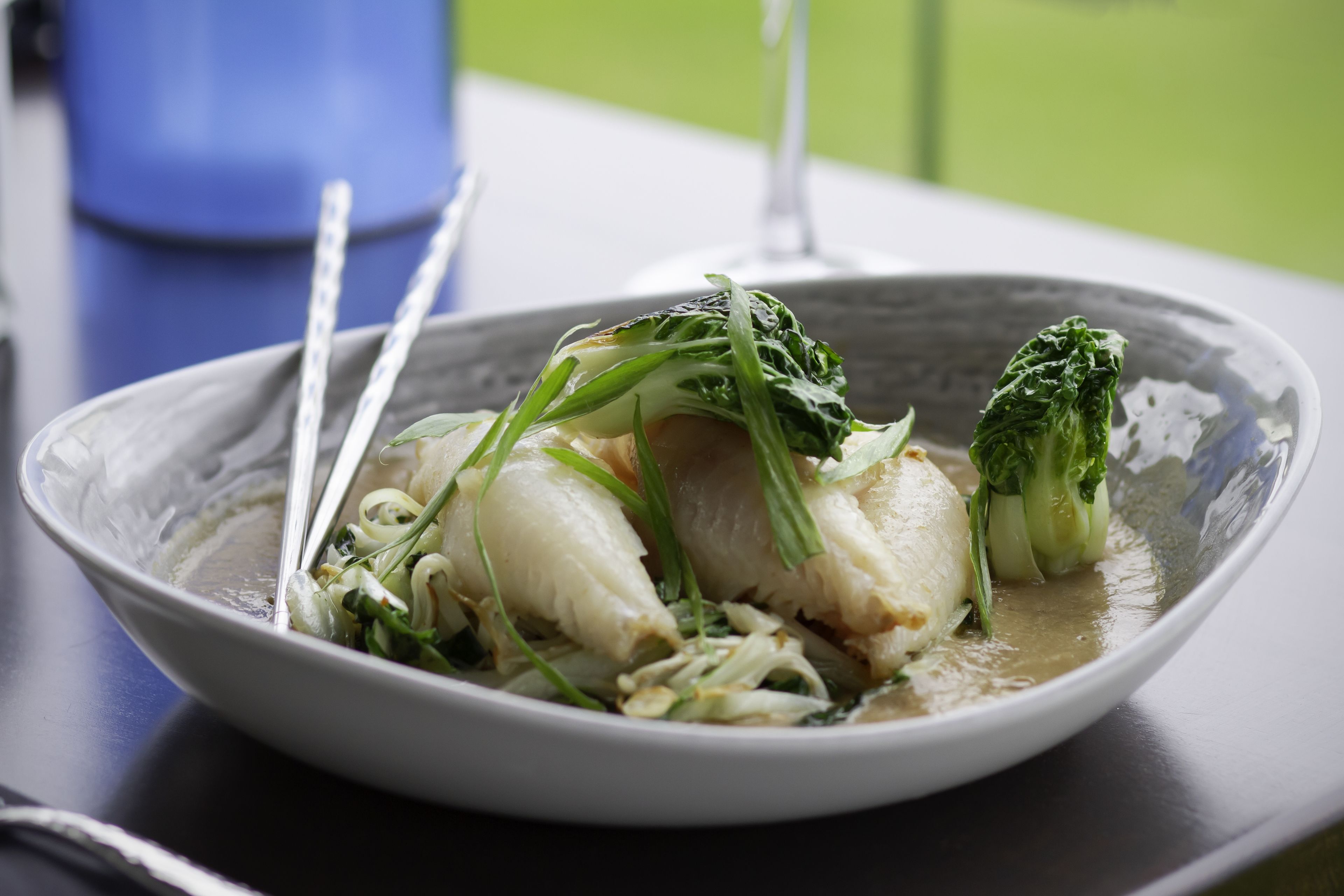 A bowl of food with chopsticks and a blue container in the background.